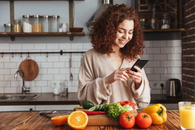 キッチンに並べた野菜と、笑顔でスマホを操作する女性