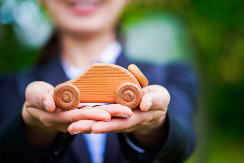 女性が手の平に木でできた車のオブジェをのせて、見せつけている