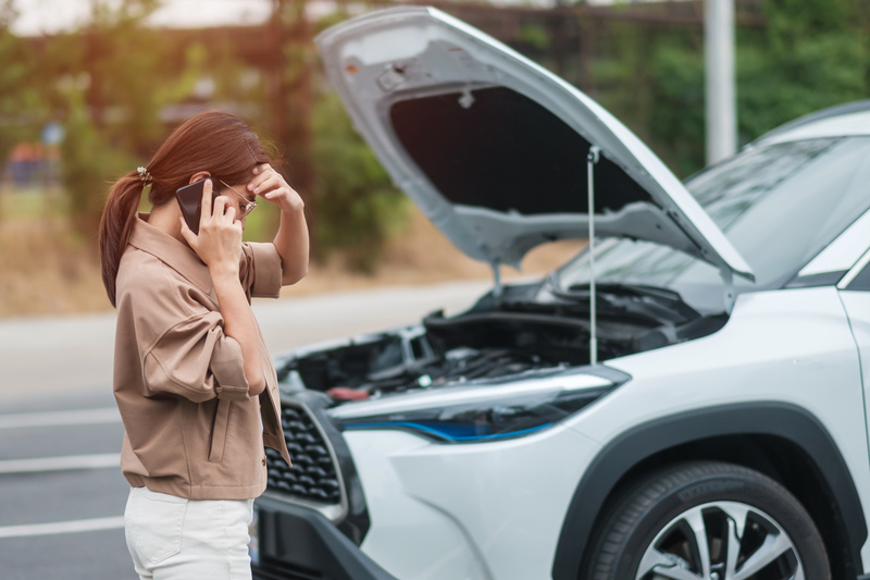 車のボンネットを開け電話をする女性